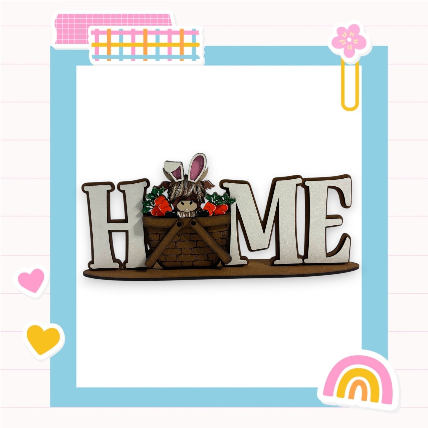 A wooden sign with the word "HOME" in large letters, featuring a small rabbit or bunny figure inside a basket. The sign is surrounded by various colorful and decorative elements, such as hearts, a rainbow, and a flower.