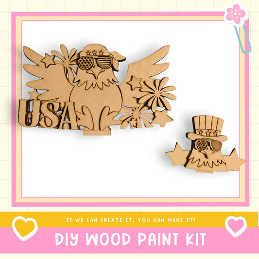 The image is a DIY wood paint kit featuring a wooden eagle and a wooden character with a hat, both adorned with stars and the word "USA" written on them.