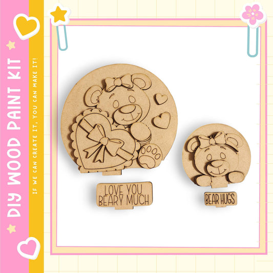 two wooden cutouts of teddy bears, one larger and one smaller, both with heart-shaped cutouts and bows. The larger teddy bear is positioned on the left side of the image, while the smaller one is on the right. The image also includes a sign that says "Love You Bear Much" and a heart-shaped sticker, which are placed below the larger teddy bear cutout.