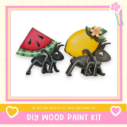 two black ant figurines carrying a watermelon and a lemon, set against a white background with a pink border.