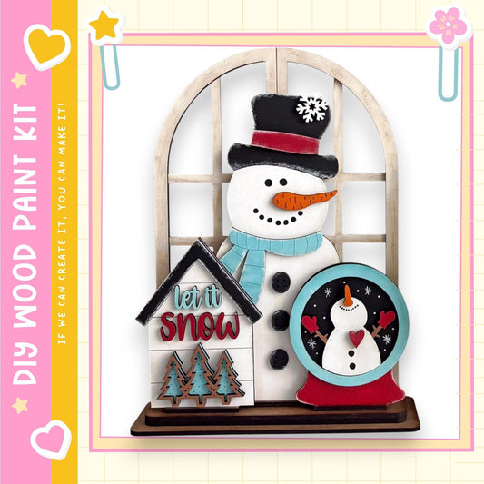 A snowman and a snow globe are displayed in a decorative arrangement, with a sign that says "let it snow" and a heart-shaped sticker.