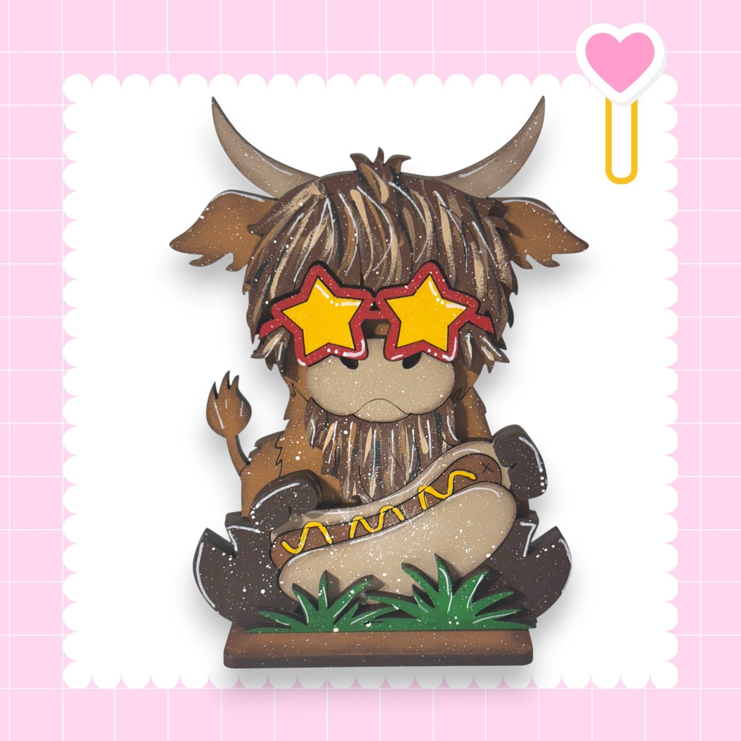A cartoon cow wearing sunglasses and holding a hot dog, set against a pink background with a heart shape.