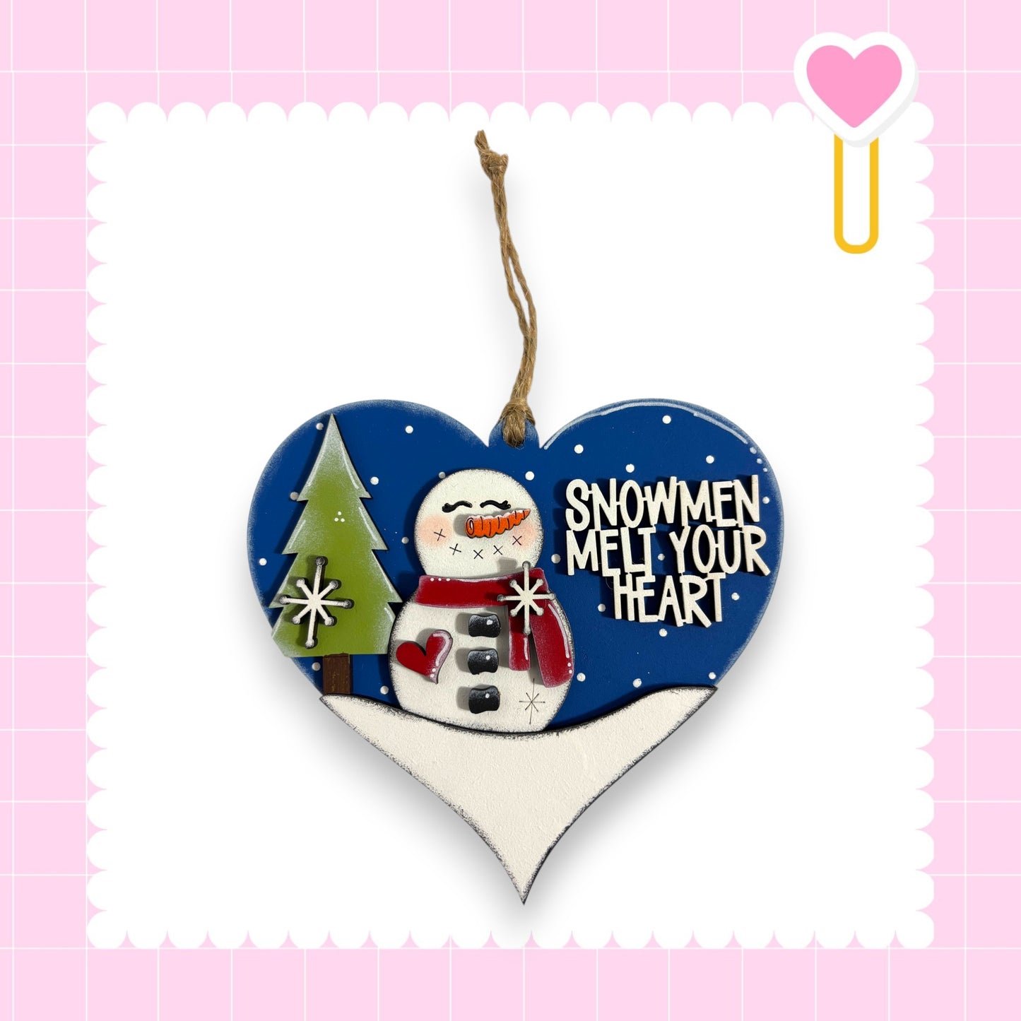 A heart-shaped ornament with a snowman and a tree, along with the text "SNOWMEN MELT YOUR HEART" written on it.