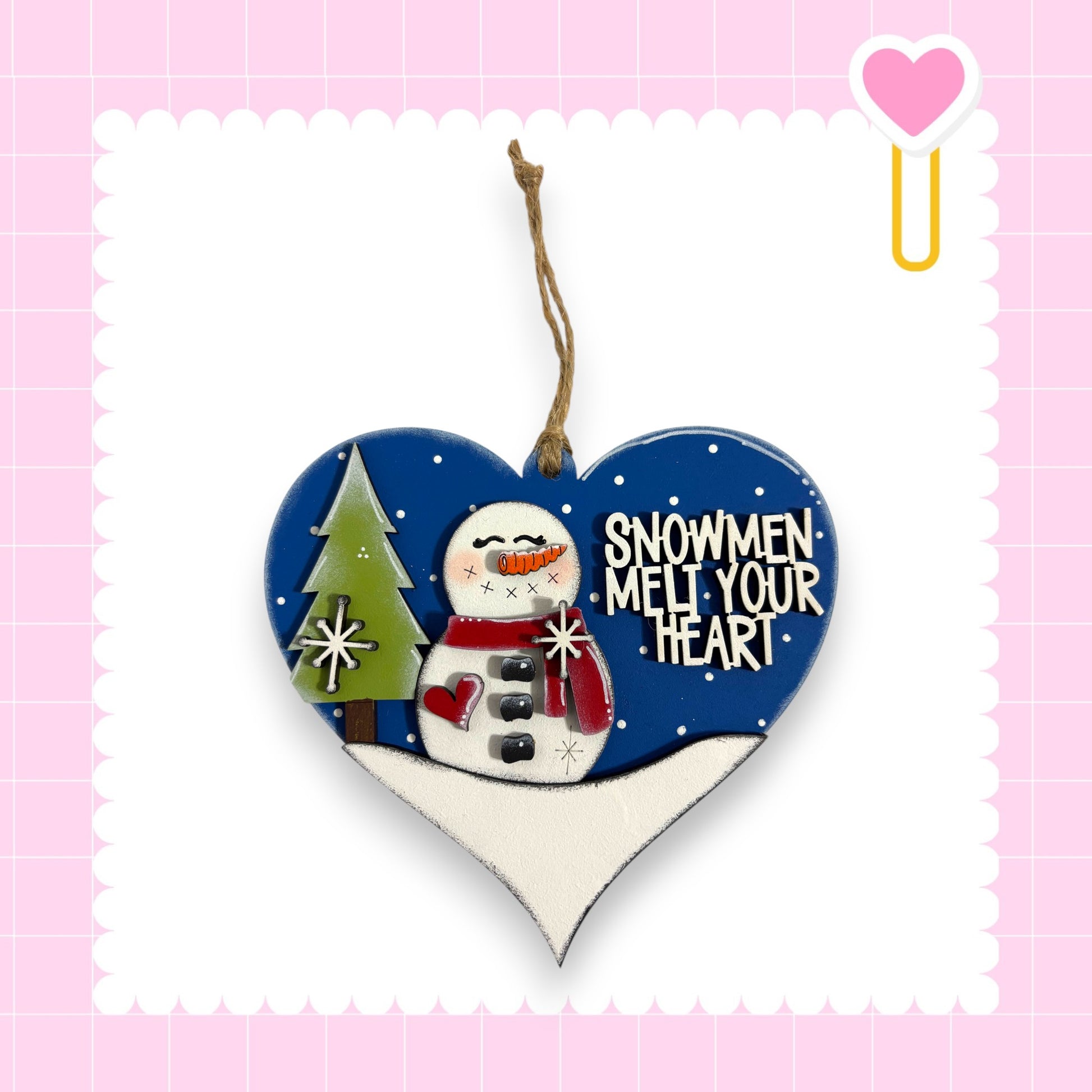 A heart-shaped ornament with a snowman and a tree, along with the text "SNOWMEN MELT YOUR HEART" written on it.
