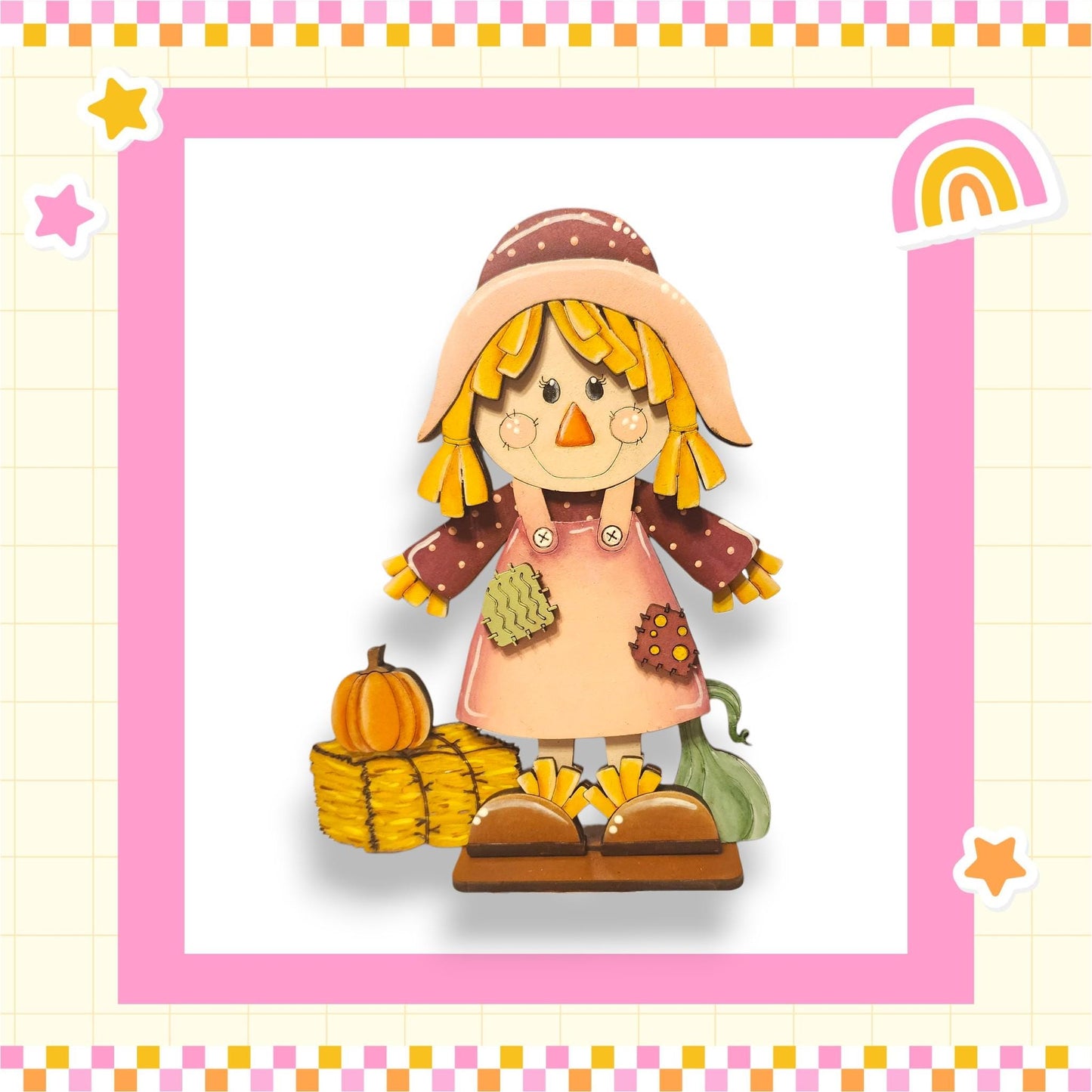 A cheerful cartoon scarecrow stands in a pink and yellow frame, surrounded by autumn-themed decorations such as a pumpkin, a rainbow, and stars.