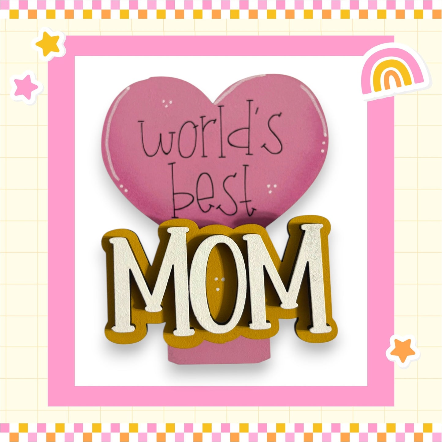 a pink heart-shaped sign with the text "world's best mom" written on it, surrounded by a pink and yellow checkered border.