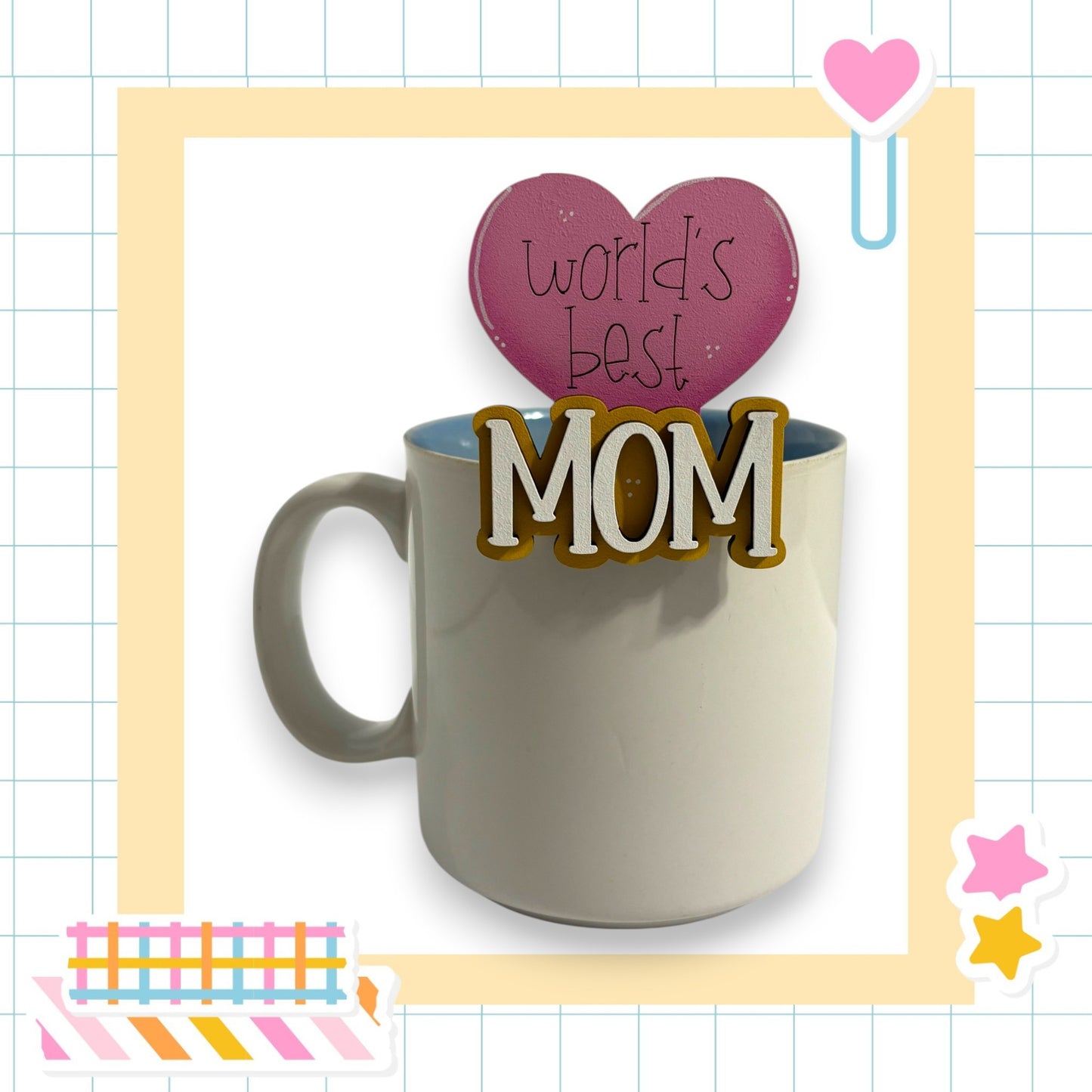 A white mug with a heart-shaped decoration on top, surrounded by various colorful and decorative elements, including a heart-shaped sticker and a pink heart-shaped object.