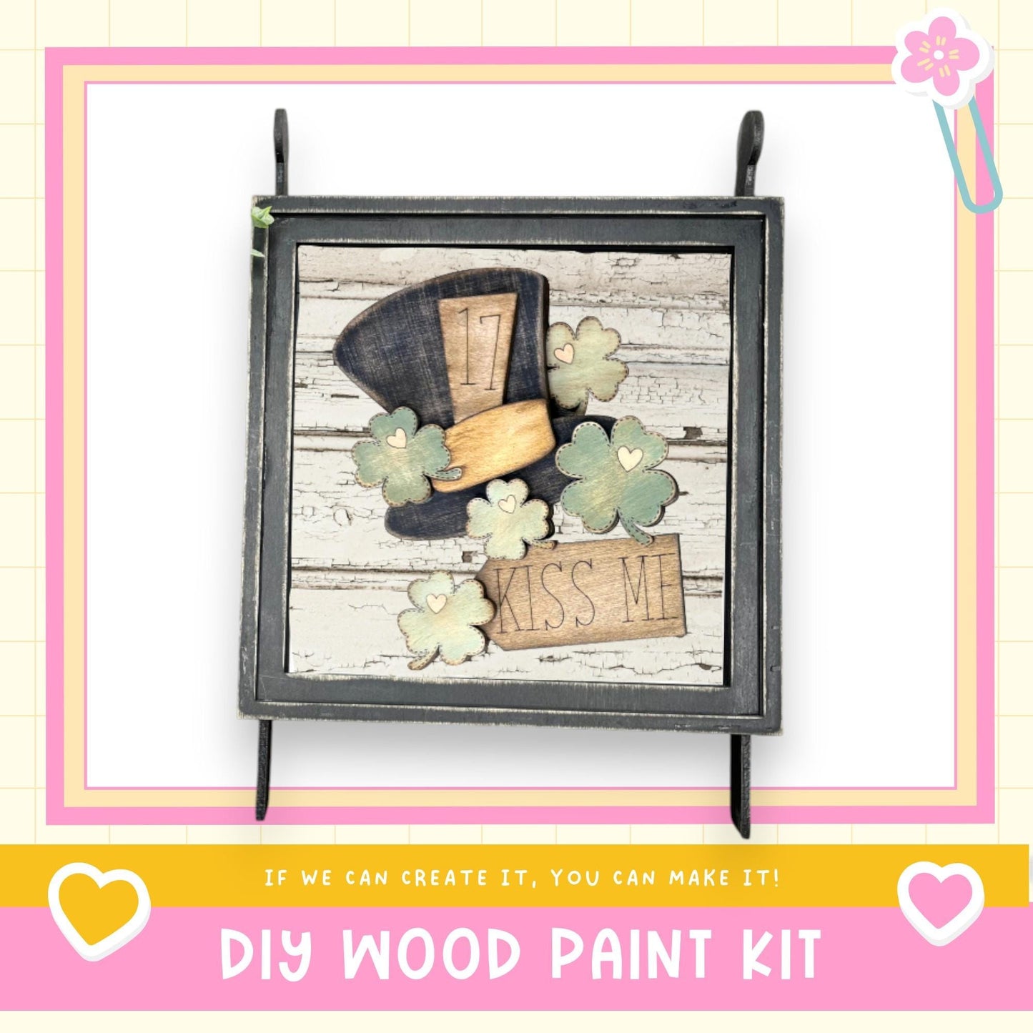 The image is a framed collage featuring a wooden frame with a black border, a wooden hat, and a sign that says "KISS ME". The collage is set against a pink and white background, and there is text at the bottom that reads "DIY WOOD PAINT KIT" and "IF WE CAN CREATE IT, YOU CAN MAKE IT!".