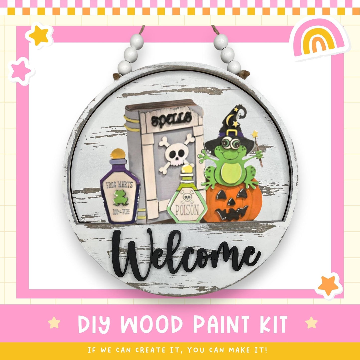 a DIY wood paint kit for creating a welcome sign. The kit includes a wooden sign with a cartoon frog, a skull and crossbones, a bottle of frog juice, and a pumpkin. The kit also includes the text "Welcome" and "DIY WOOD PAINT KIT" along with a rainbow and stars.