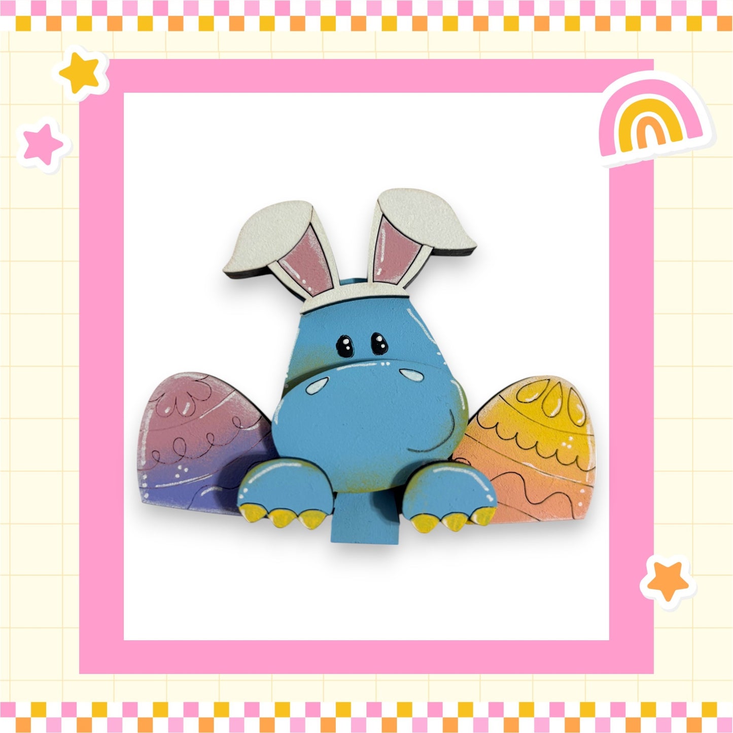 A blue cartoon rabbit with large ears and a smiling face is sitting in the center of a pink and yellow checkered border, surrounded by Easter eggs and stars.