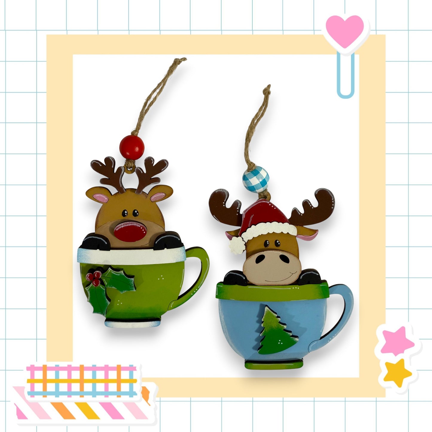 two Christmas ornaments, each in a cup, with reindeer or moose heads inside. The cup on the left has a green color, while the cup on the right has a blue color. The ornaments are hanging from strings, and there are additional decorative elements in the background, such as a heart and stars.