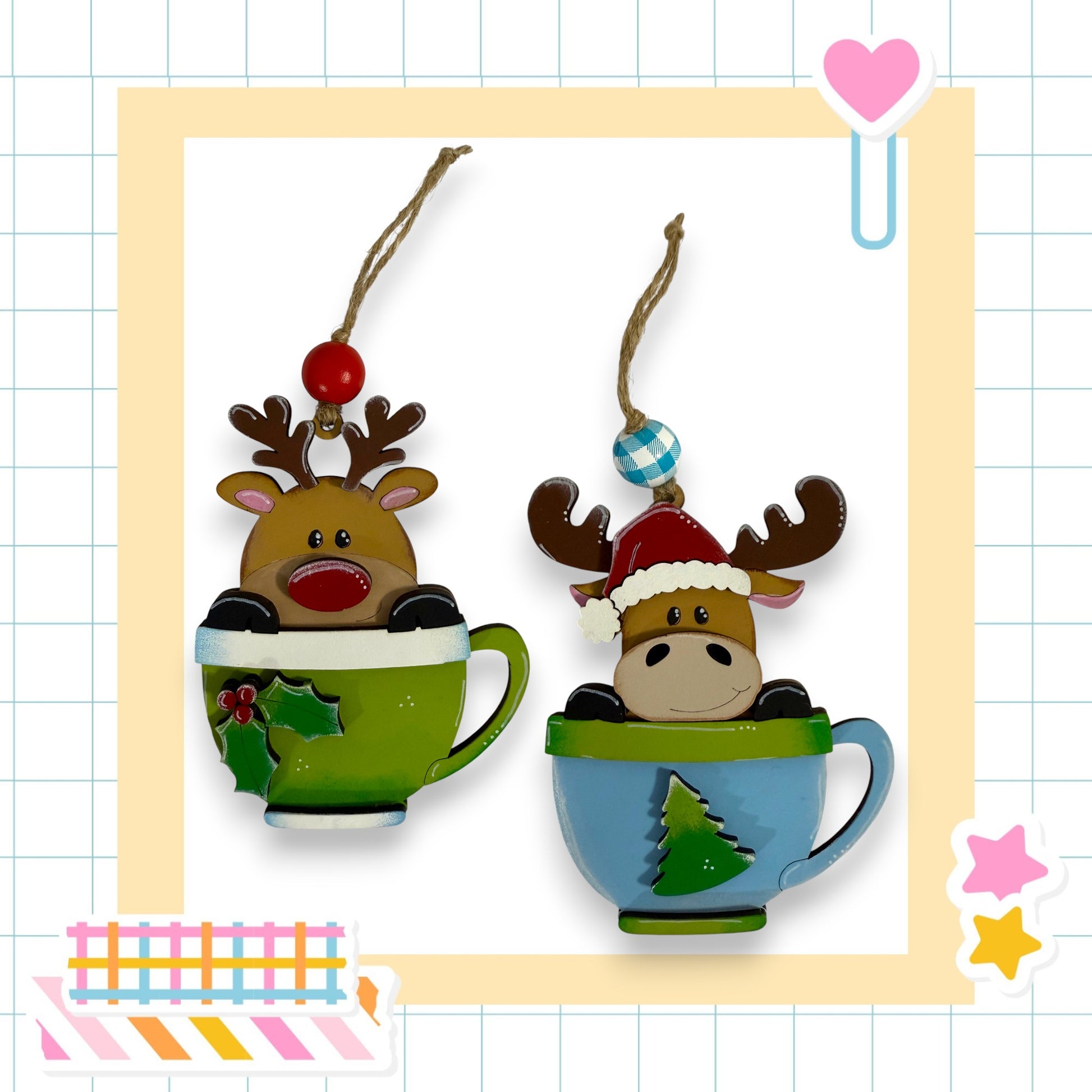 two Christmas ornaments, each in a cup, with reindeer or moose heads inside. The cup on the left has a green color, while the cup on the right has a blue color. The ornaments are hanging from strings, and there are additional decorative elements in the background, such as a heart and stars.