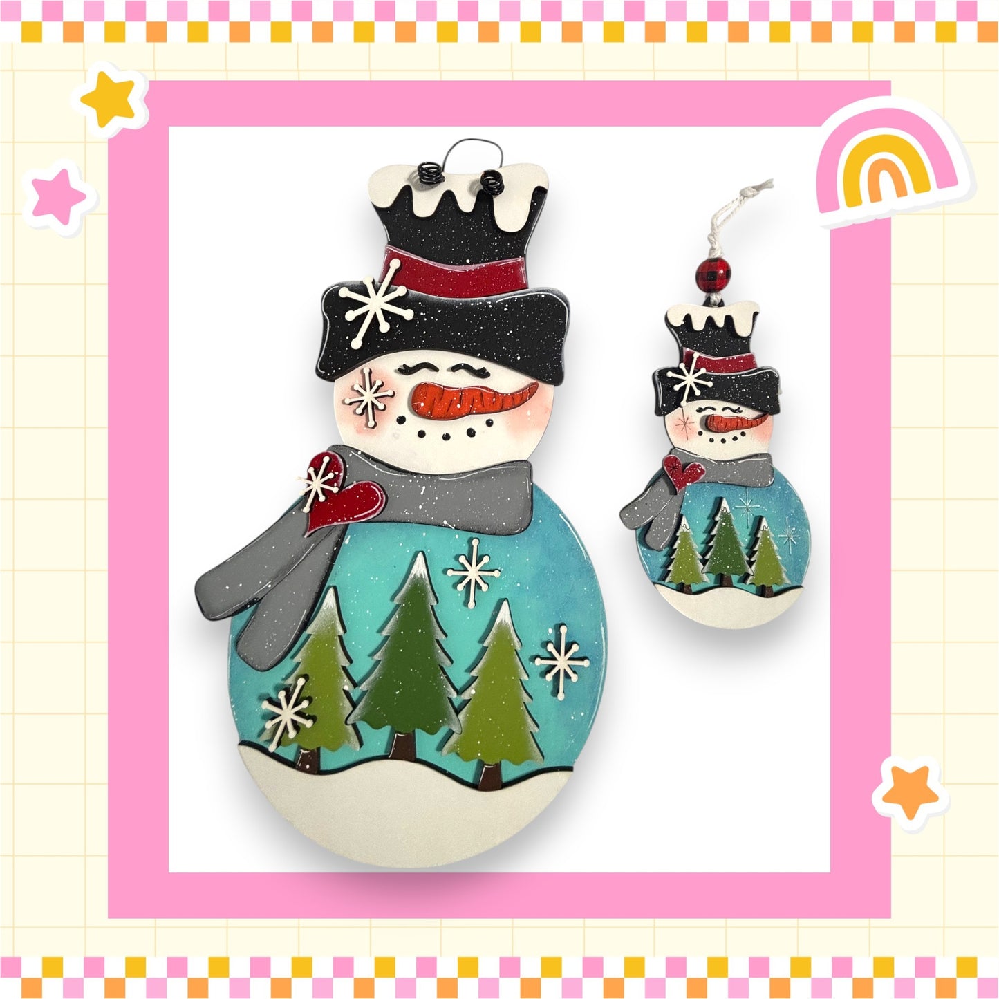 A snowman ornament with a blue body, green trees, and a red bow, set against a pink and yellow background with stars and a rainbow.