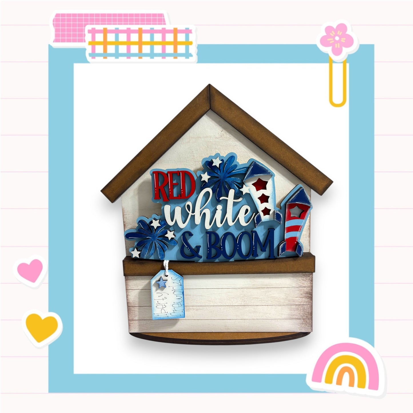 A wooden house-shaped object with the text "RED white & BOOM" written on it, surrounded by various colorful and decorative elements such as hearts, a rainbow, and a flower.