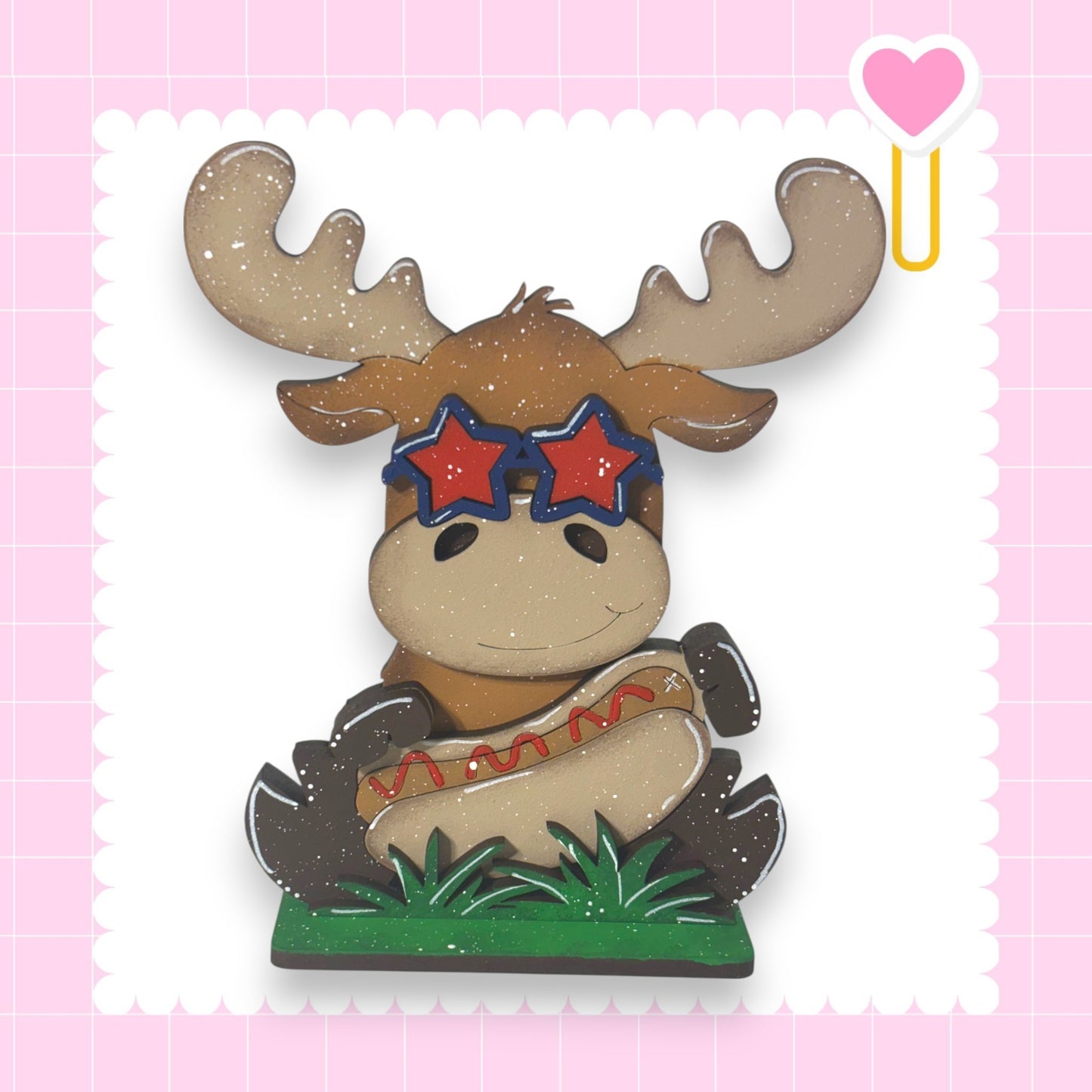 A cartoon moose wearing sunglasses and holding a hot dog, set against a pink background with a heart shape.
