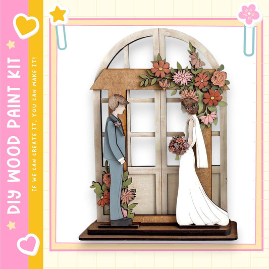 A wooden wedding cake topper depicting a bride and groom standing in front of a floral arch.