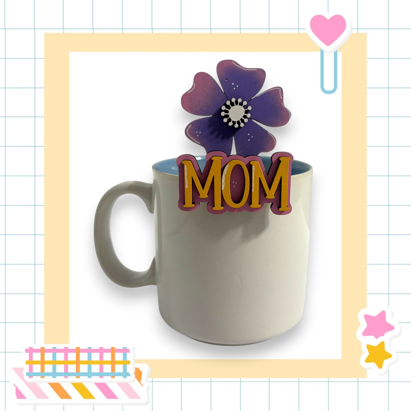 A white mug with the word "MOM" written on it, placed on a table surrounded by various colorful and decorative elements.