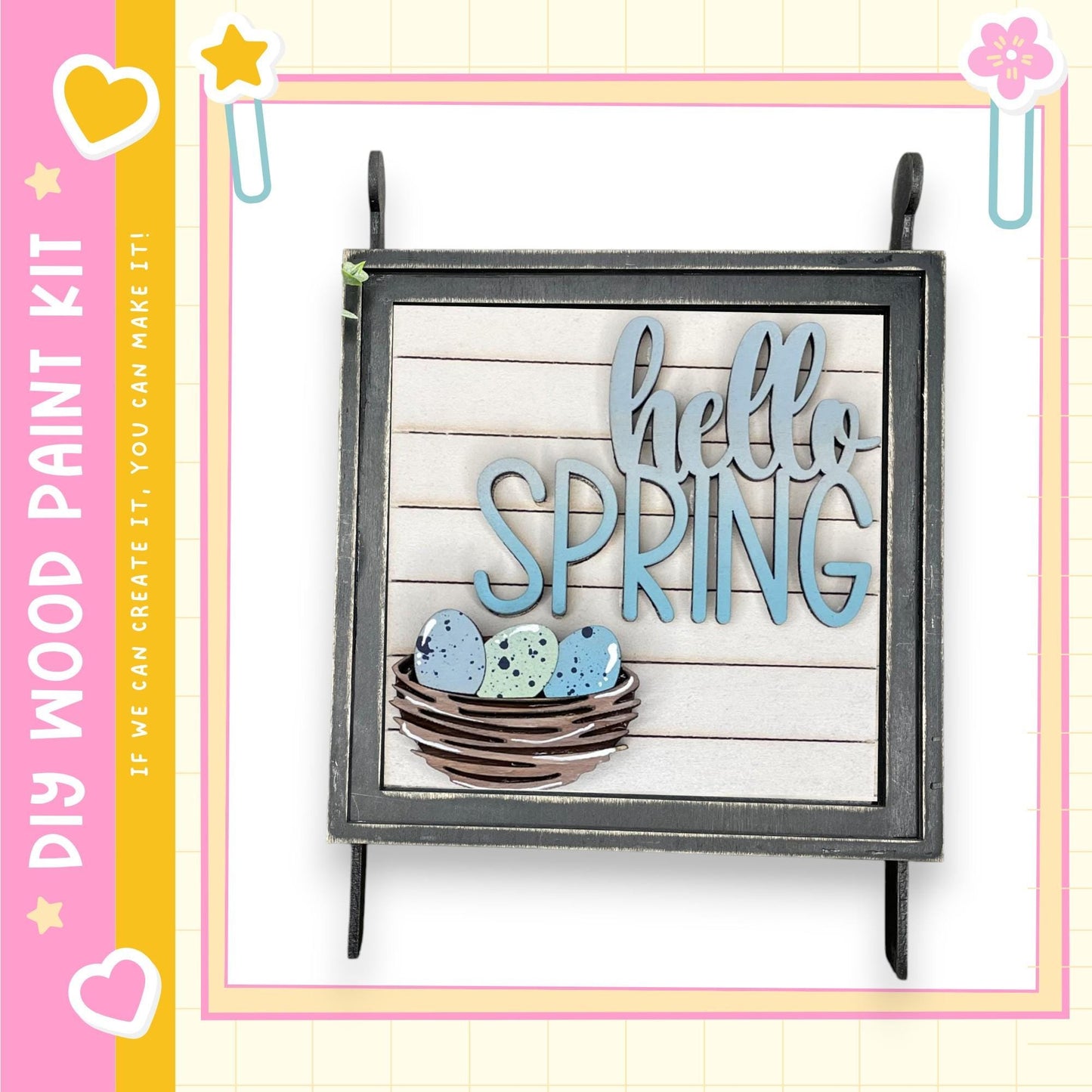 a wooden sign with the text "Hello Spring" displayed on it, along with a basket of eggs and a heart. The sign is hanging on a wall, and the background has a pink and yellow color scheme.