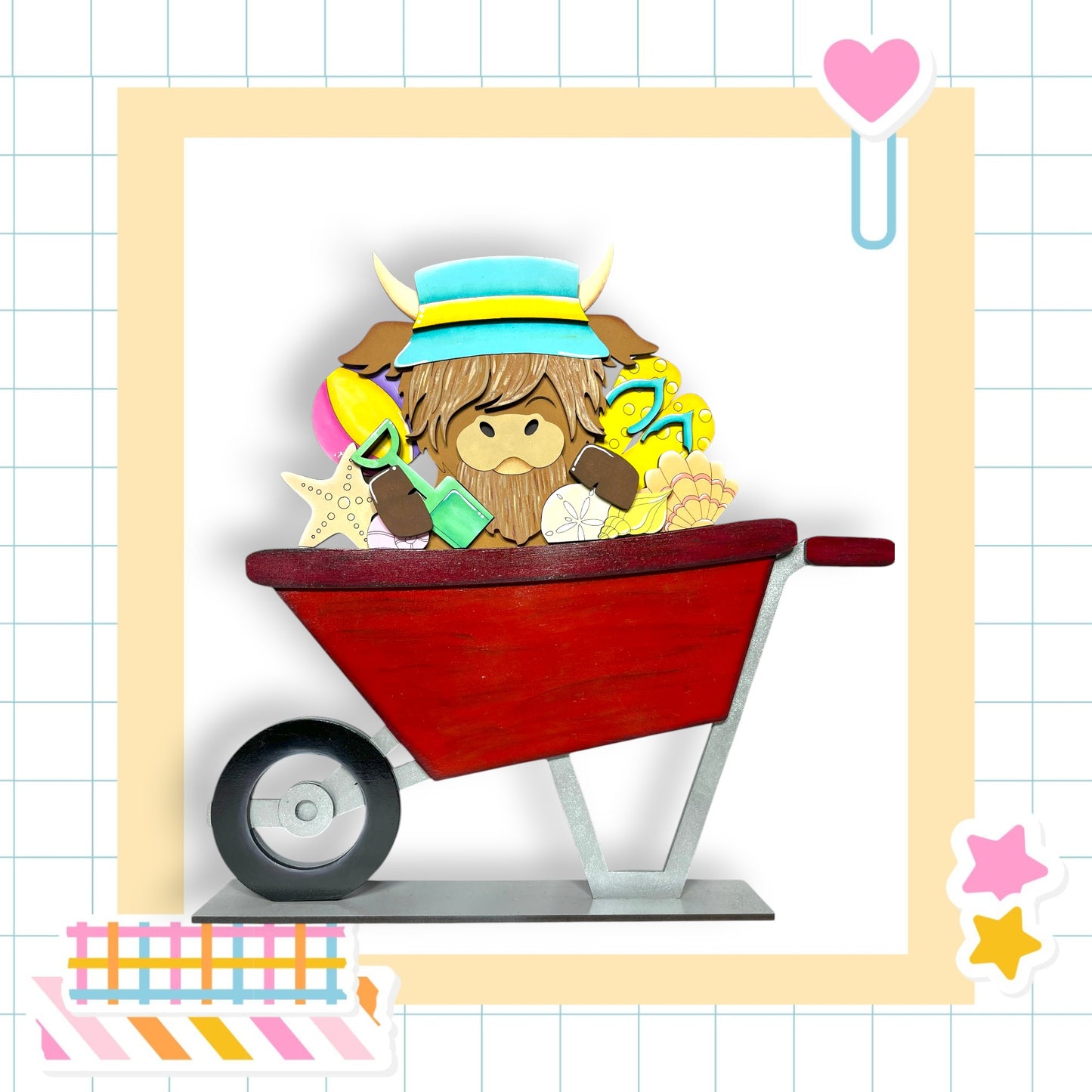 A red wheelbarrow filled with various objects, including a yellow hat, a blue hat, and a pink heart, is surrounded by colorful stickers and a heart-shaped clip.