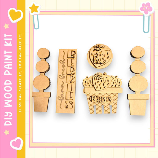a collection of wooden shapes, including a cactus-shaped object, a strawberry-shaped object, and a heart-shaped object, all of which appear to be part of a DIY paint kit.