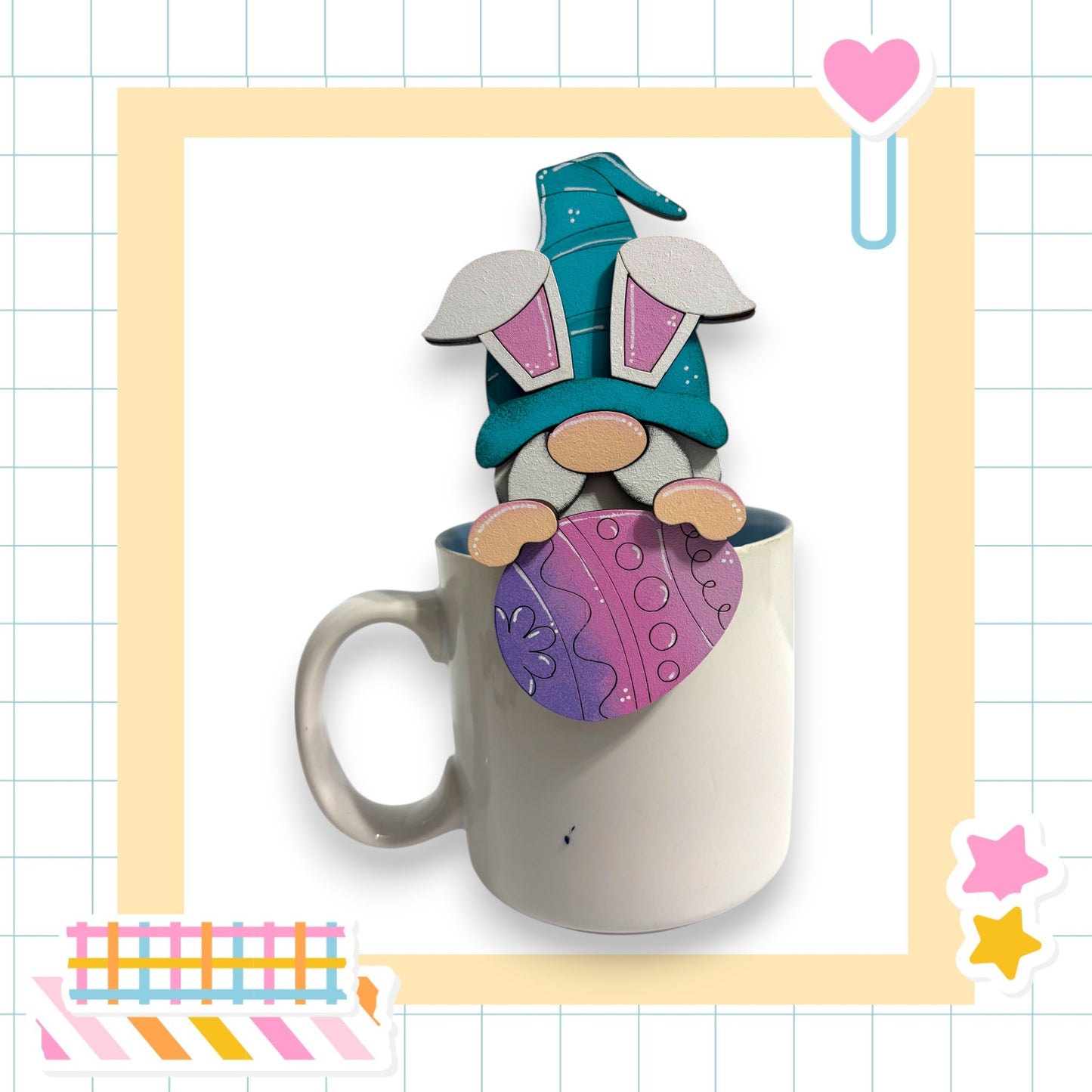 A whimsical ceramic mug with a gnome figurine peeking out from inside, set against a grid background with various colorful stickers and a heart-shaped object.