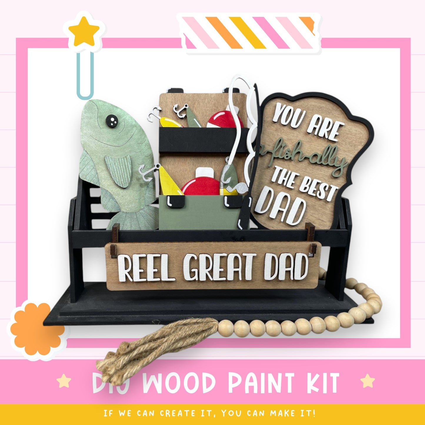 The image is a DIY wood paint kit with a wooden sign that says "REEL GREAT DAD" and a fish-shaped decoration. The kit appears to be made of wood and includes various tools and materials for painting.