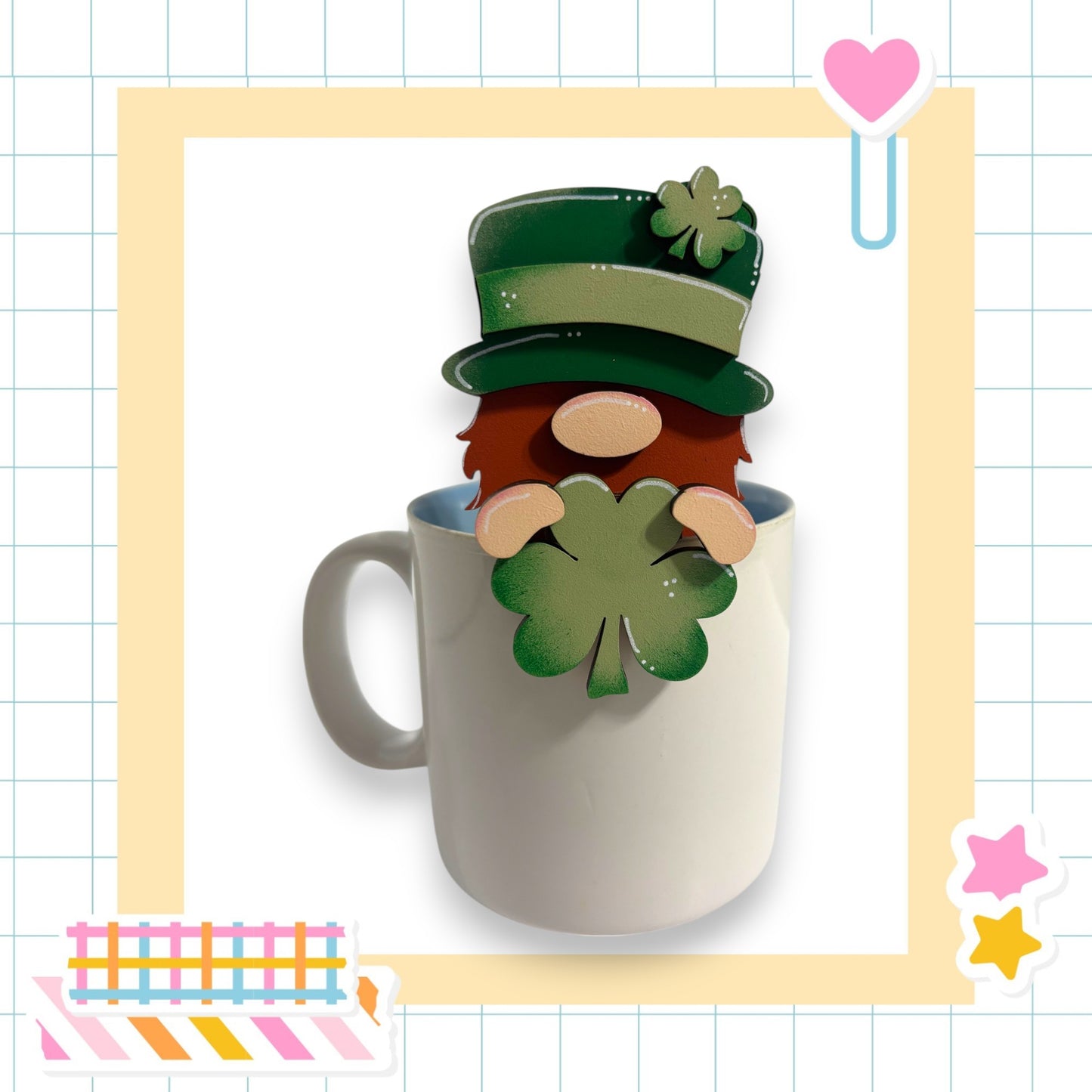 A cartoon mug with a smiling face and a clover leaf, set against a grid background with various colorful stickers.
