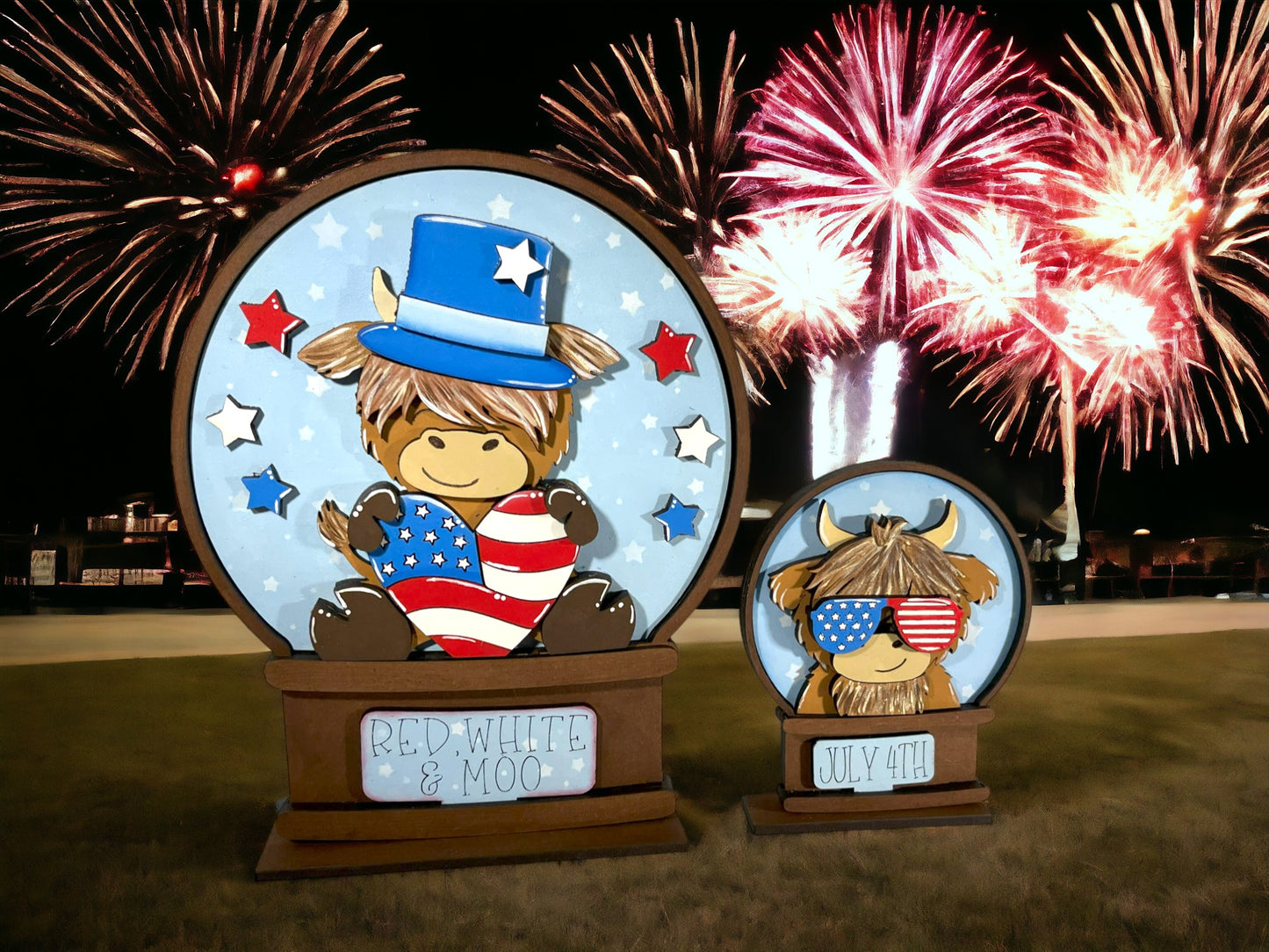 two wooden cutouts of cartoon cows, one larger and one smaller, set against a backdrop of a fireworks display.