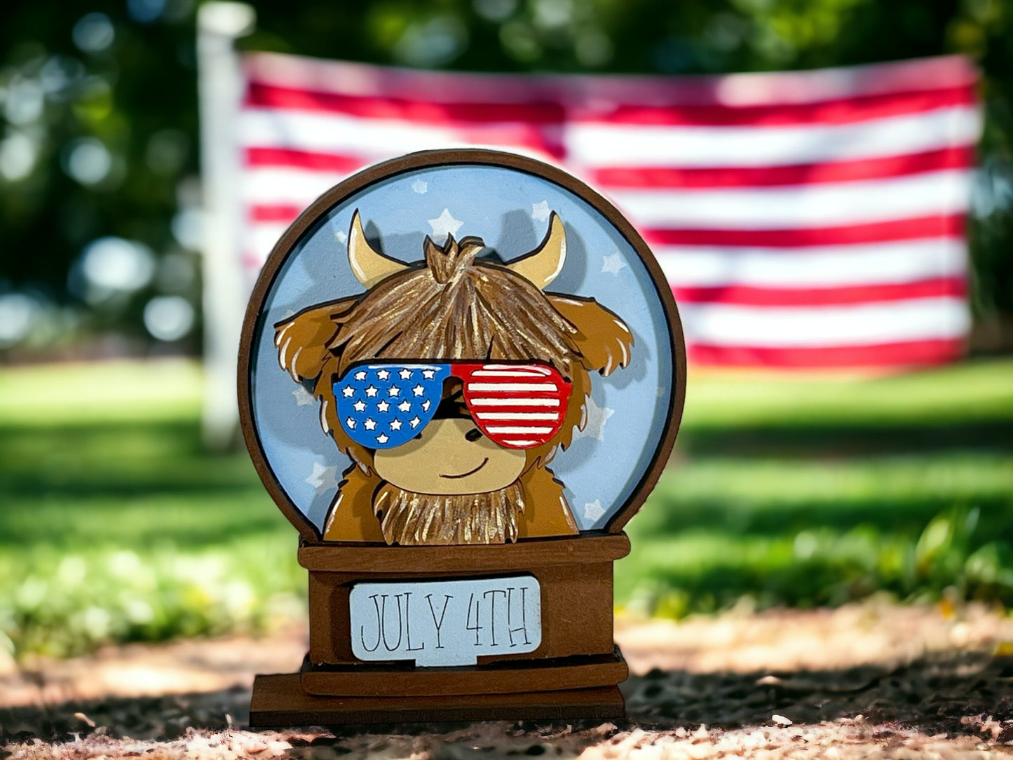 A wooden figurine of a cow wearing sunglasses and an American flag in the background.