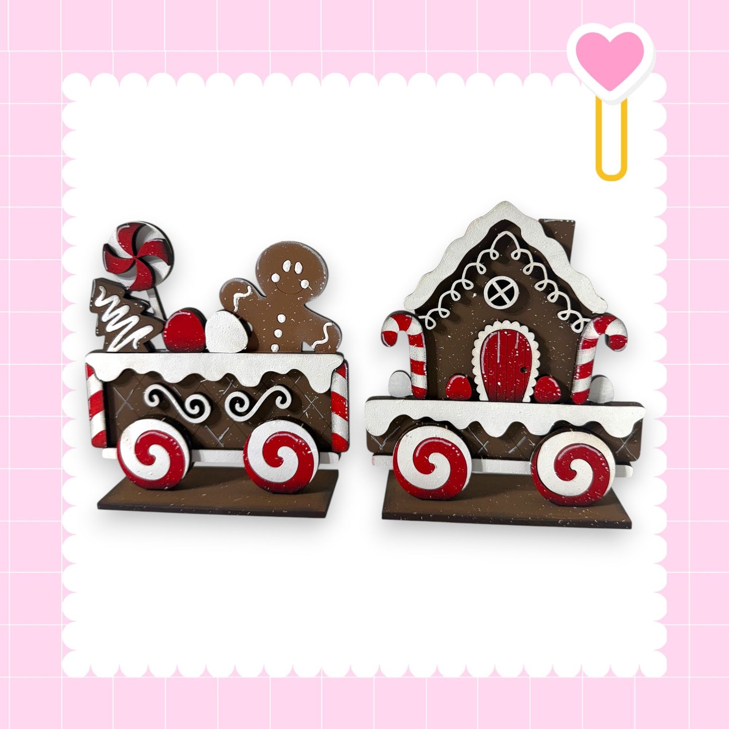 two wooden toy train cars, each decorated with candy and gingerbread houses, set against a pink background.