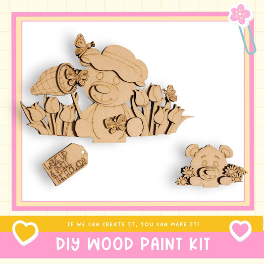 The image is a DIY wood paint kit featuring a wooden bear and flowers, with a tag that says "WALK UP AND SMELL THE FLOWERS".