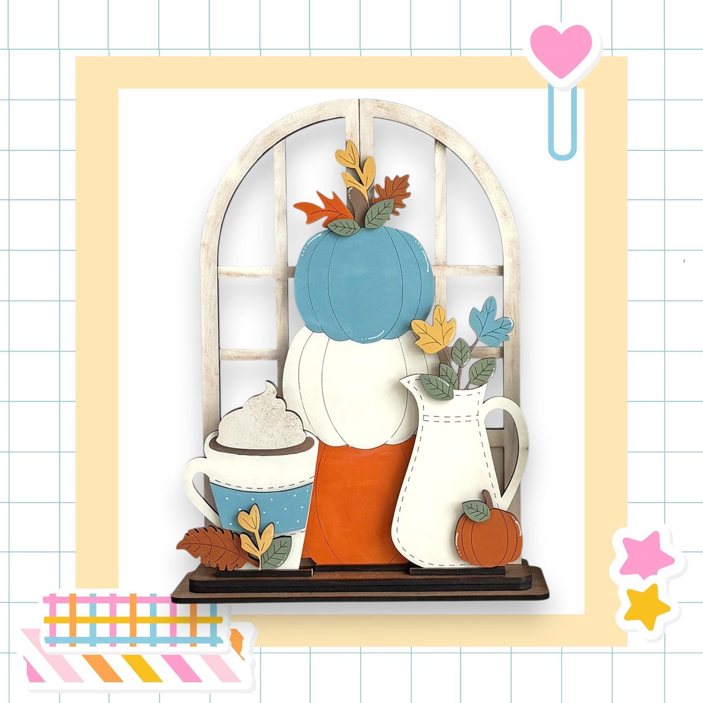 A wooden shelf with various fall-themed decorations, including a blue pumpkin, a white pitcher, a blue mug with whipped cream, and a white vase with a pumpkin. The shelf is set against a white background with a grid pattern.