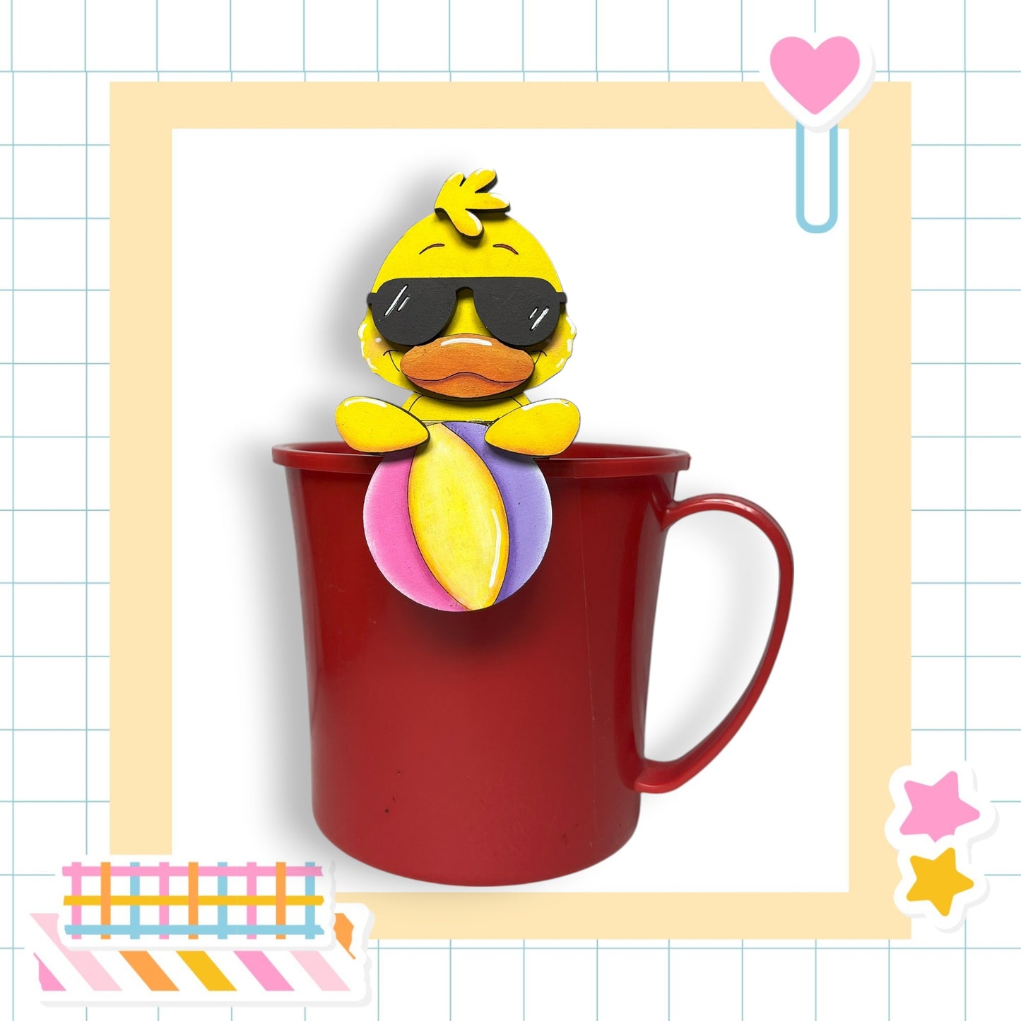 A yellow duck wearing sunglasses is perched on a red mug, set against a grid background with various colorful stickers and a heart-shaped clip.