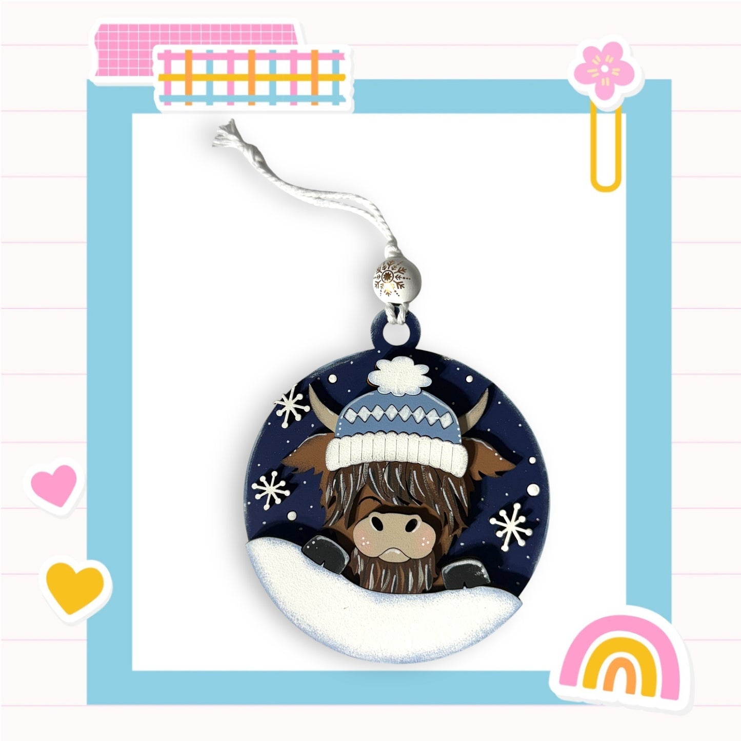 A decorative ornament featuring a cow wearing a winter hat and surrounded by snowflakes, with a colorful frame and various other decorative elements in the background.