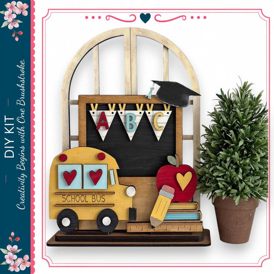a DIY kit with a school bus, a chalkboard, a potted plant, and a pencil, all arranged on a shelf.
