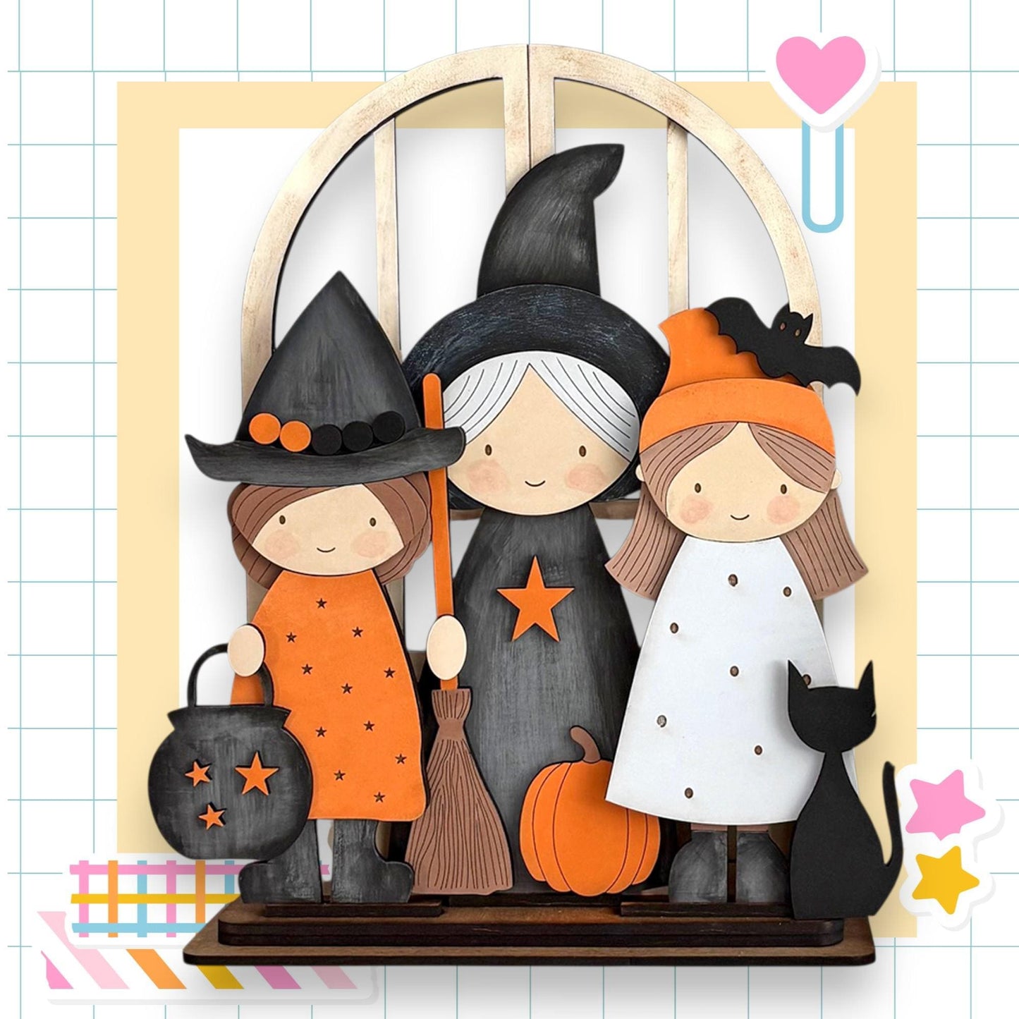 A Halloween-themed display featuring three cartoon-style girls dressed as witches, with a black cat and a pumpkin as part of the scene.