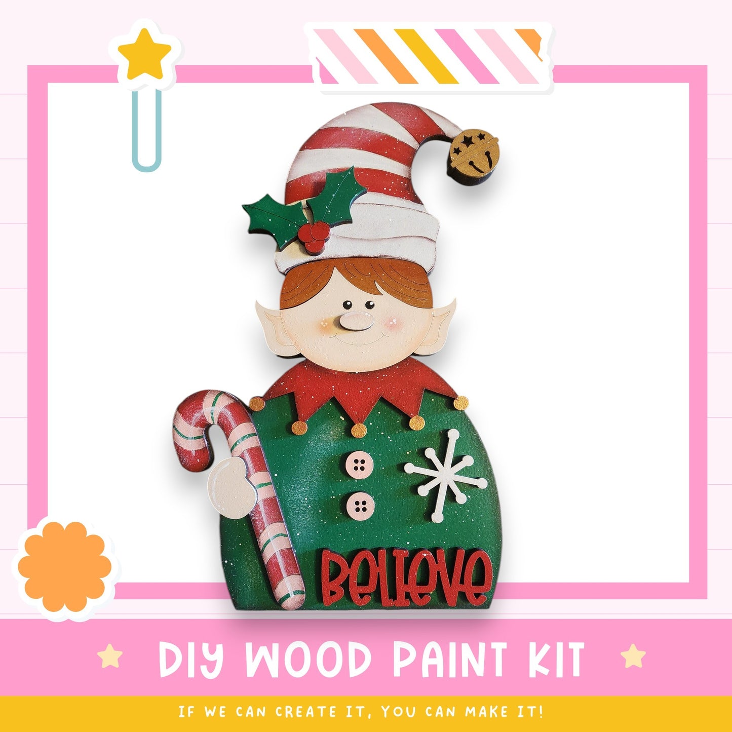 a DIY wood paint kit for creating a wooden elf decoration. The kit includes a wooden elf figure, a candy cane, and the word "Believe" written on the elf's chest. The kit is presented in a pink and white color scheme, with a star decoration on the left side. The text "DIY WOOD PAINT KIT" is displayed at the bottom of the image, along with the phrase "IF WE CAN CREATE IT, YOU CAN MAKE IT!"
