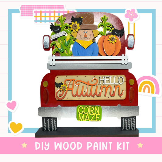 The image is a colorful and whimsical DIY wood paint kit featuring a scarecrow, corn maze, and fall-themed decorations.
