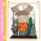 A wooden toy moose holding a fishing rod and standing next to a Christmas tree, with a pink and yellow border around the image.