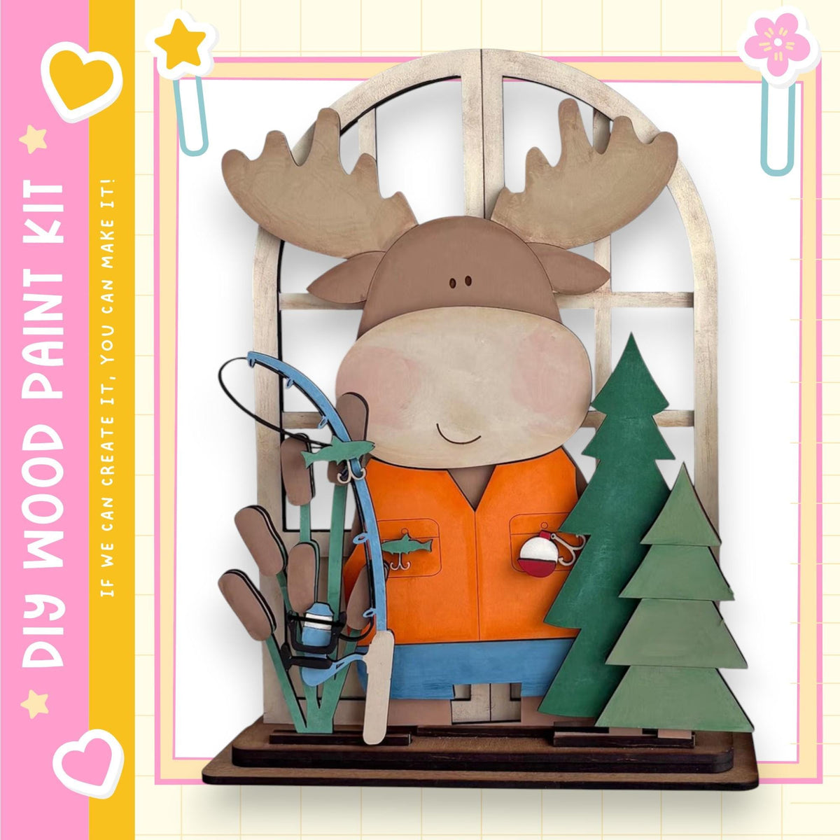 A wooden toy moose holding a fishing rod and standing next to a Christmas tree, with a pink and yellow border around the image.
