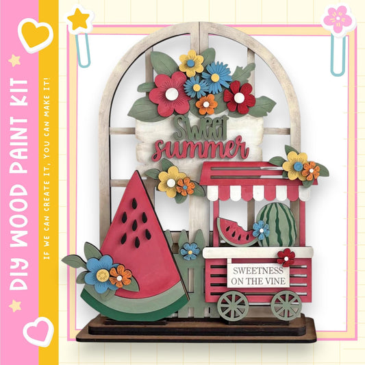 The image is a colorful and whimsical display featuring a wooden wagon, a watermelon, and various flowers and leaves. The wagon is decorated with a sign that reads "Sweet summer" and has a "Sweetness on the vine" sign on it. The overall scene is vibrant and cheerful, with the wagon and wagon cart as the main focal points.