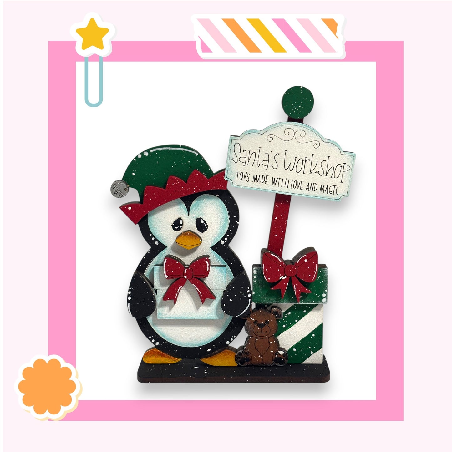 A wooden toy penguin wearing a Santa hat and holding a gift box, standing next to a sign that says "Santa's Workshop Toys Made with Love and Magic".