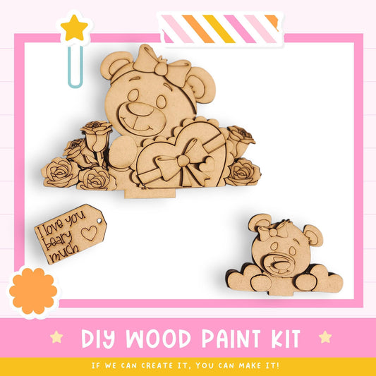 The image is a DIY wood paint kit featuring a wooden teddy bear and a smaller wooden bear, along with a heart-shaped box and a tag. The kit appears to be designed for creating wooden toys or decorations.
