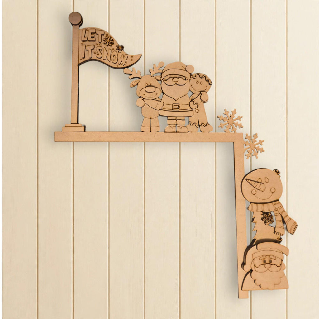 A wooden cutout of Santa Claus and other Christmas-themed characters, including a snowman and a reindeer, is mounted on a wooden shelf against a white wall.