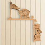 A wooden cutout of Santa Claus and other Christmas-themed characters, including a snowman and a reindeer, is mounted on a wooden shelf against a white wall.