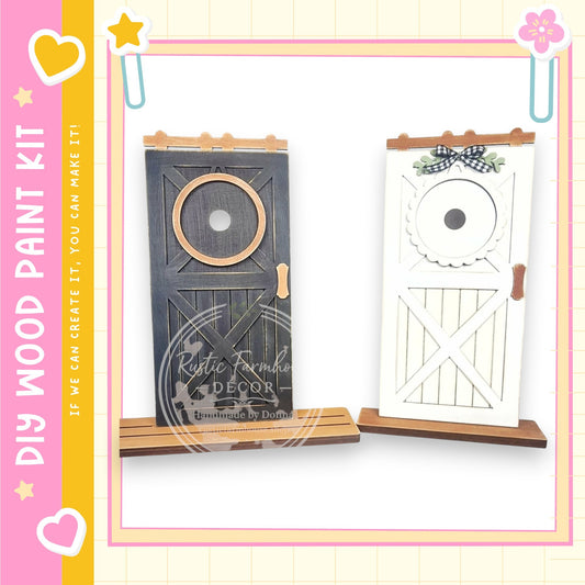 two wooden doors, one black and one white, with decorative elements such as a bow and a star on top. The doors are displayed on a wooden stand, and the image includes text that reads "My Wood Paint Kit" and "If we can create it, you can make it".