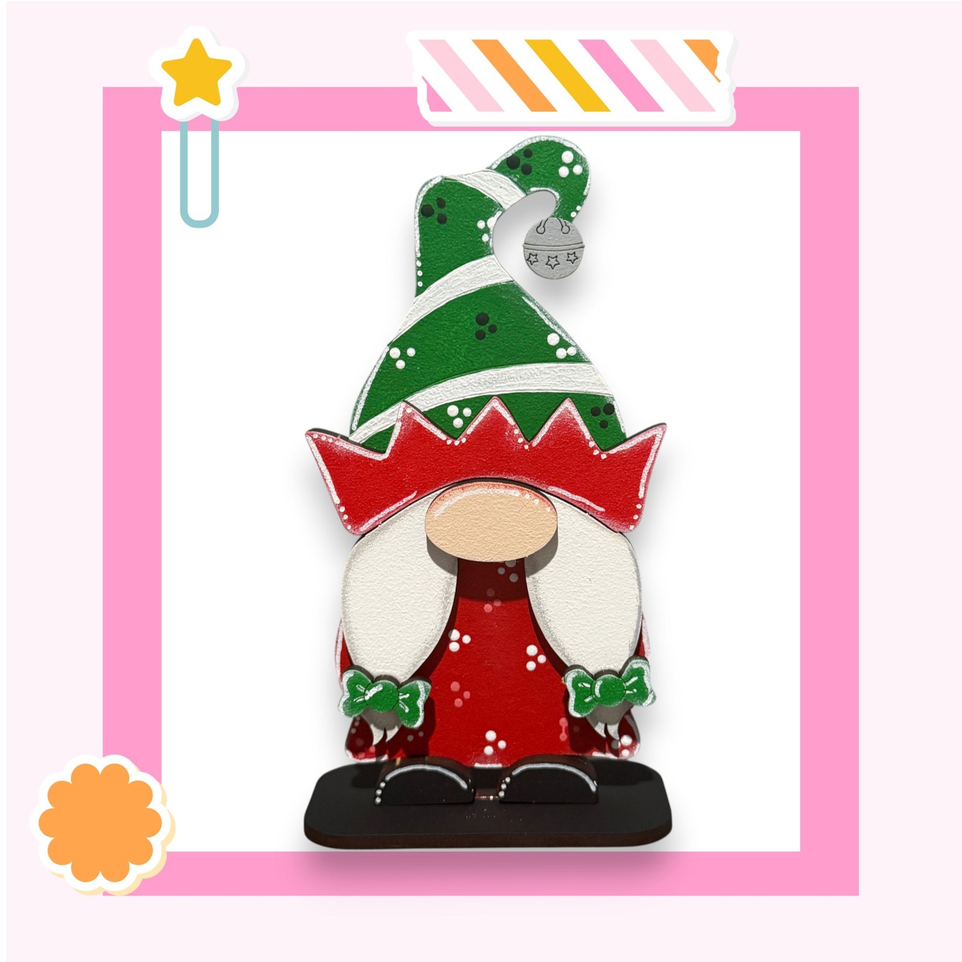 A colorful gnome figure wearing a green hat with white polka dots and a red bow, standing on a black base against a pink background.