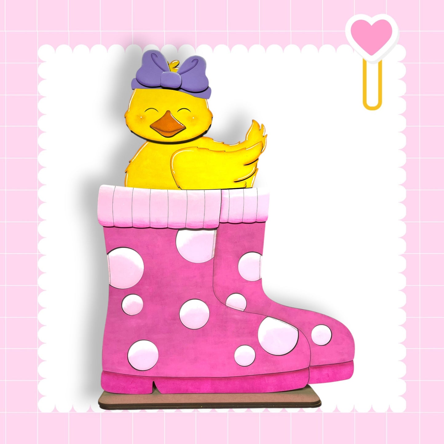 A yellow duck wearing a purple bow sits atop a pink polka-dotted boot, with a pink heart-shaped object hanging from the boot.