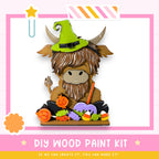 A wooden paint kit featuring a cartoon cow wearing a witch's hat, surrounded by Halloween-themed decorations such as candy and pumpkins.