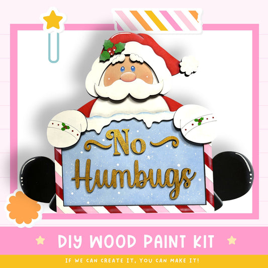 a DIY wood paint kit for creating a "No Humbs" sign, with a Santa Claus figure holding the sign.